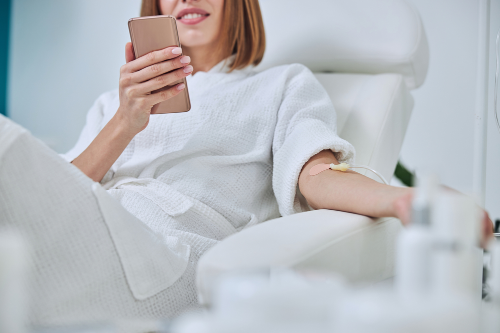 Woman looking at her phone while getting iv therapy after travel